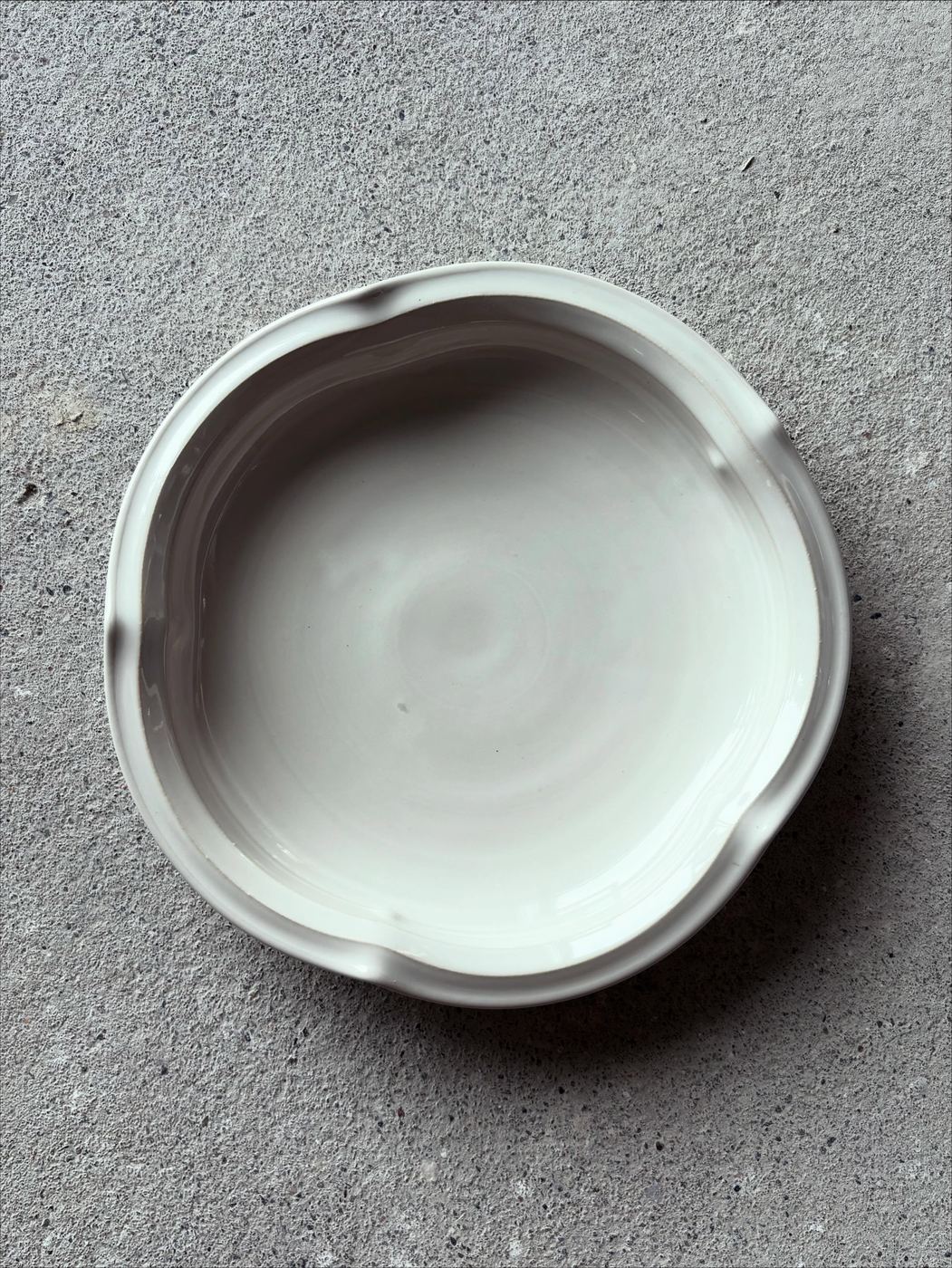 A large sculptural white serving dish on a gray concrete surface