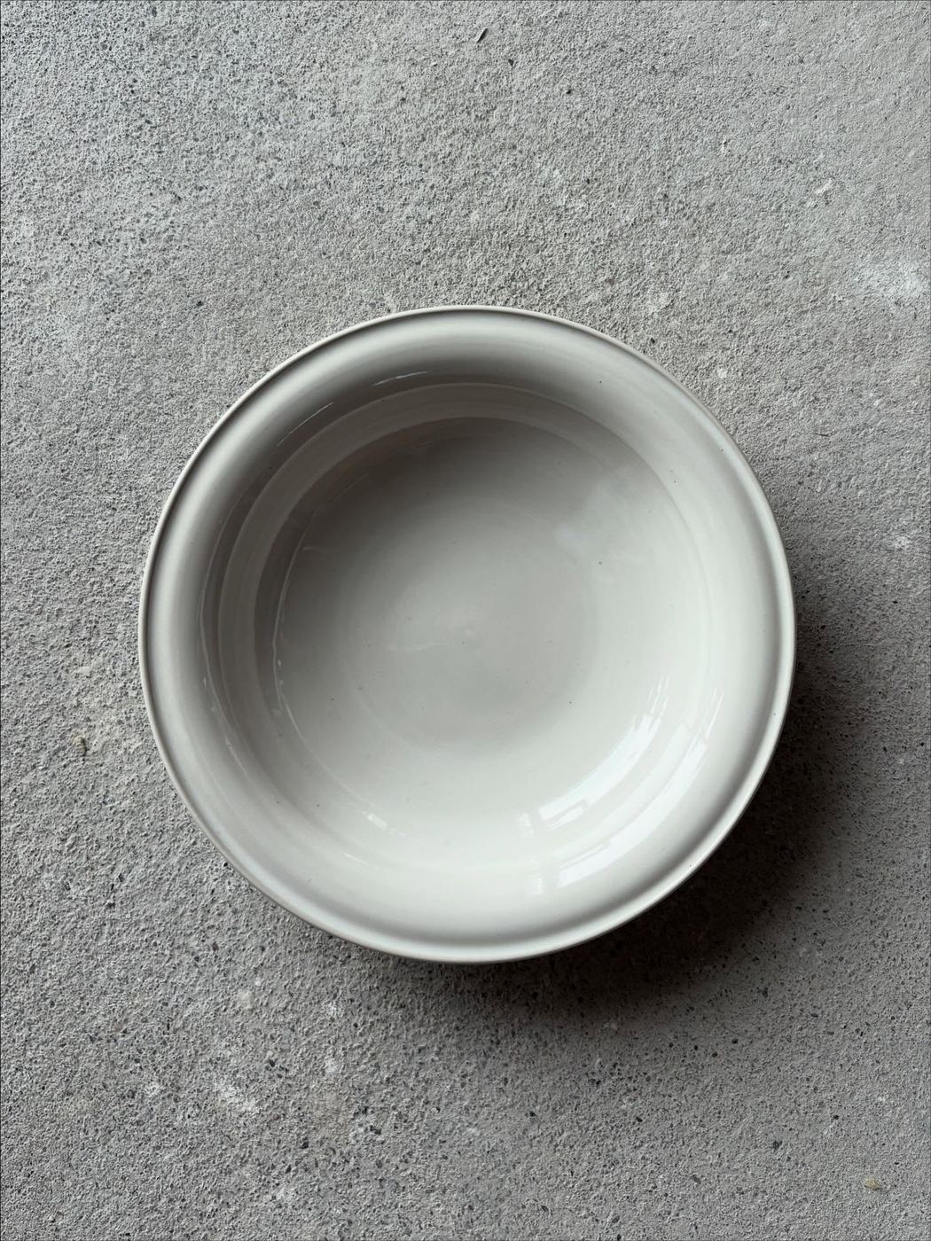 A minimal white bowl with an irregular rim on concrete