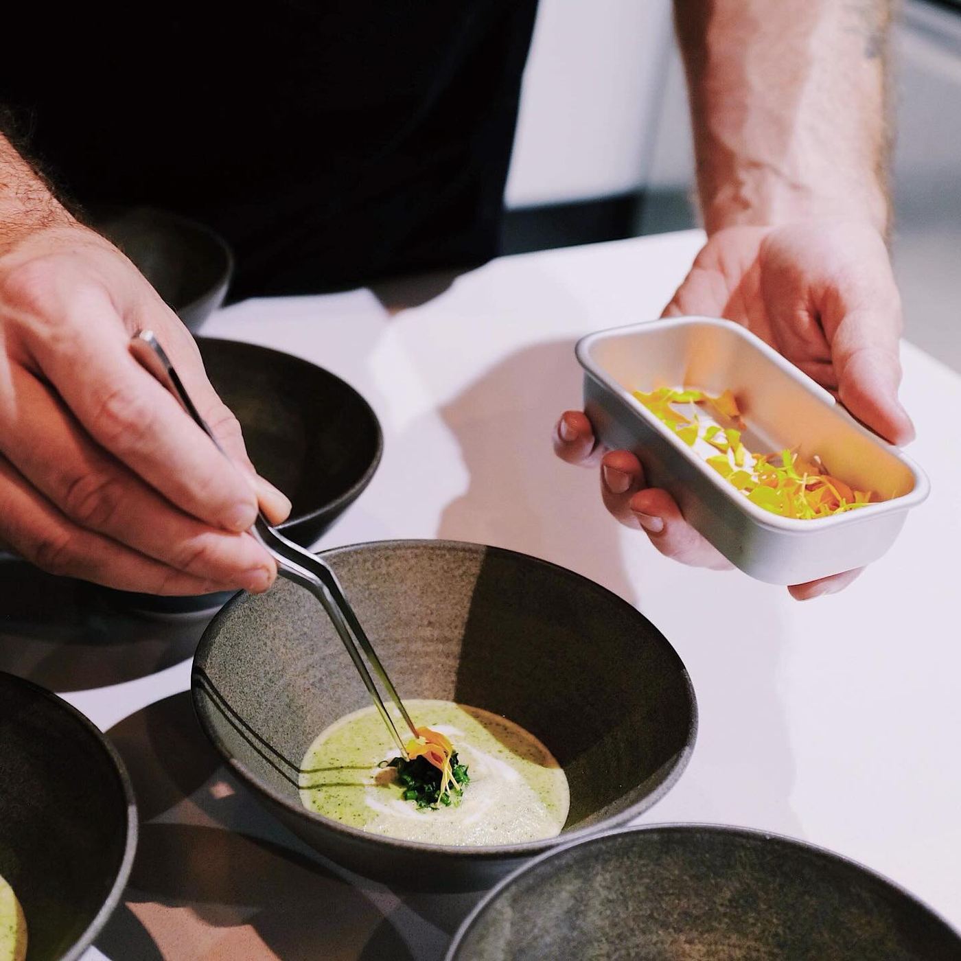 A chef placing a garnish into a dark ceramic bowl during service