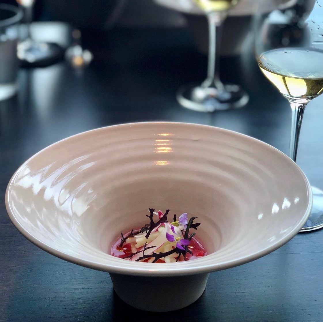 A composed course in a pale footed ceramic bowl beside a wine glass