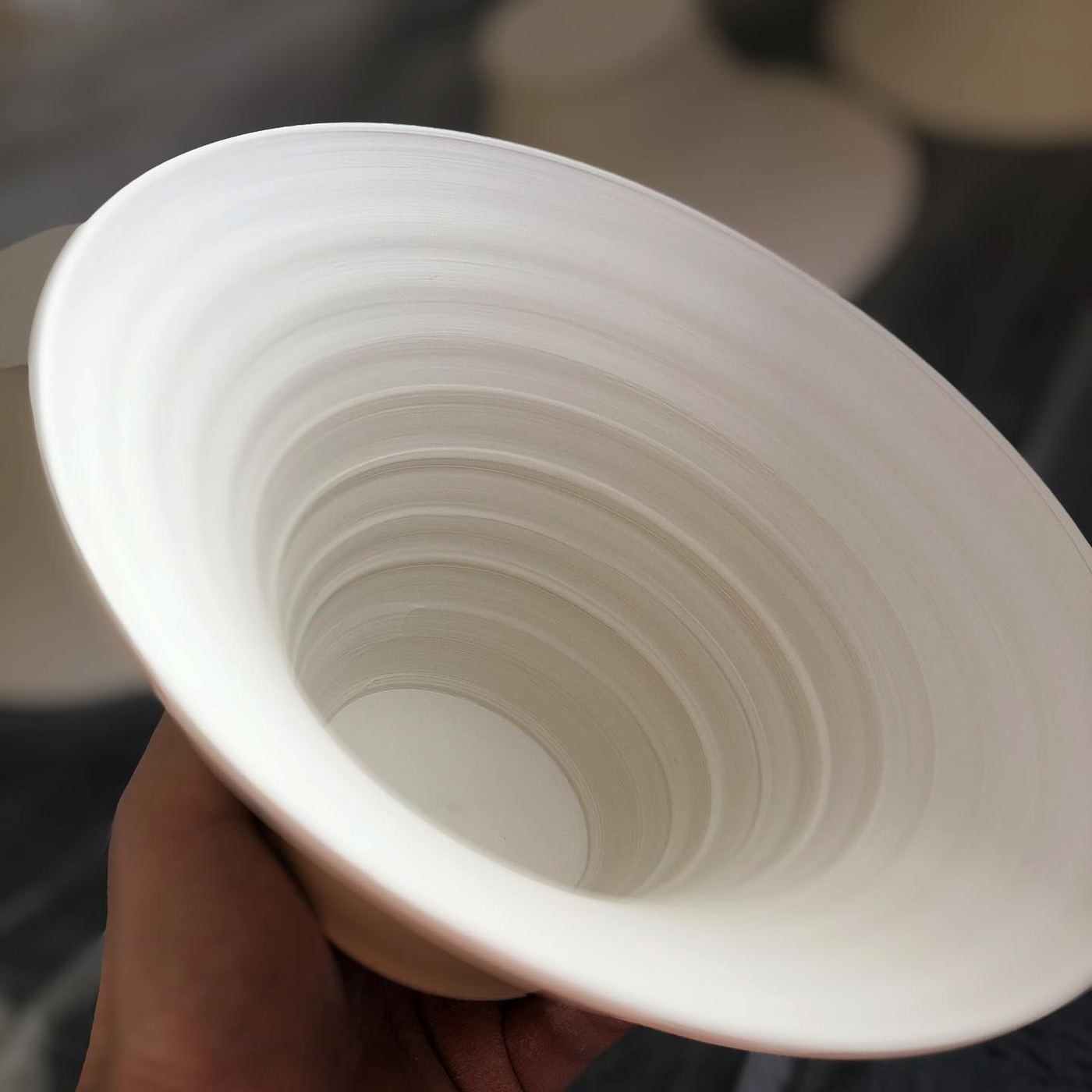 A freshly thrown white ceramic bowl held in hand