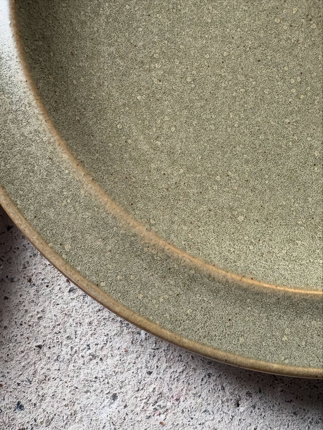 Close-up of a speckled semi-matte green glaze on overlapping ceramic plates