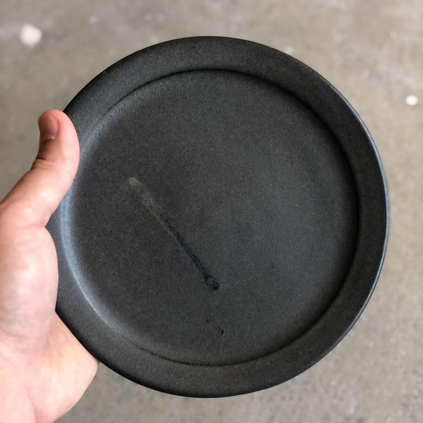 Hand holding a matte black ceramic cake plate
