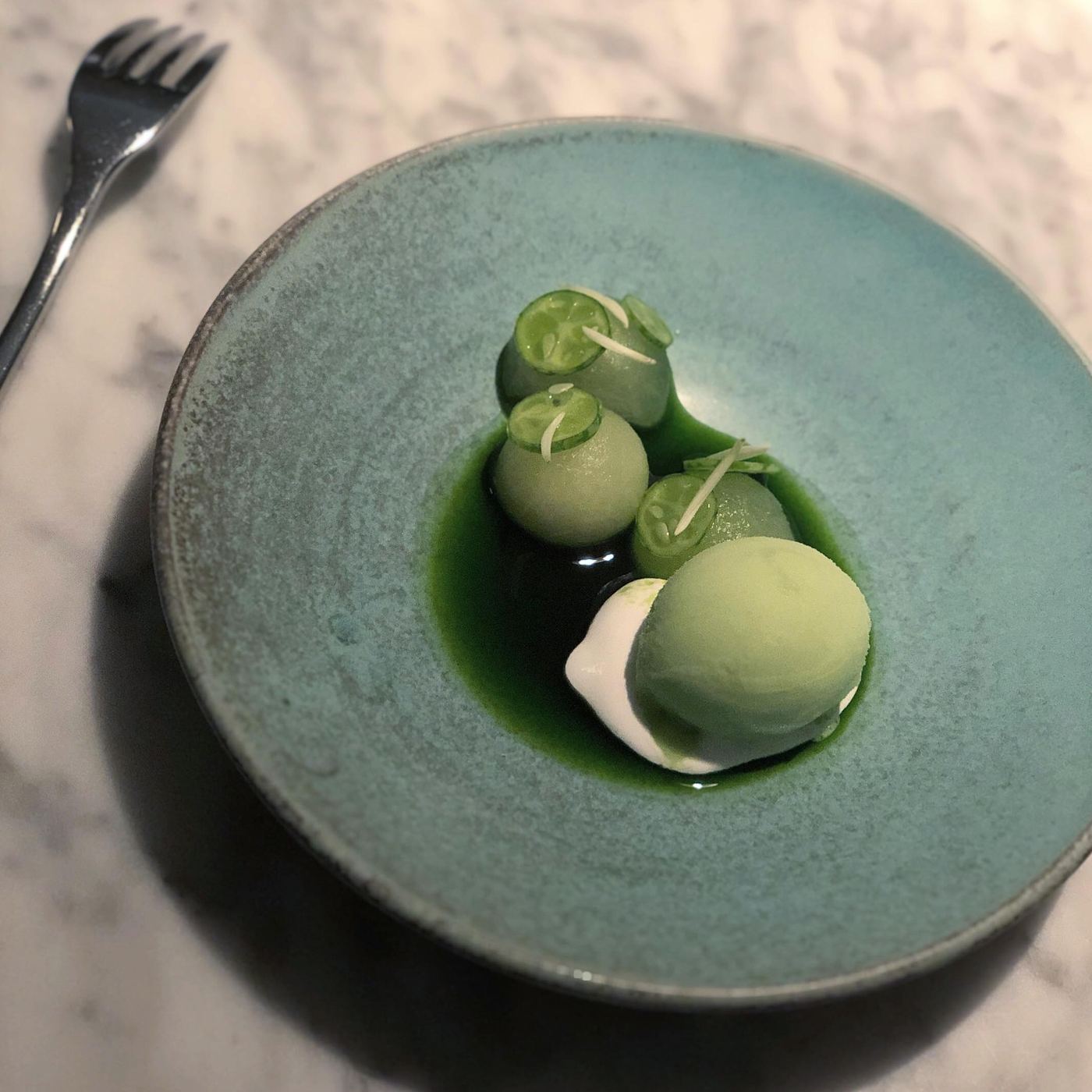 Green dessert plated in a blue-green ceramic bowl at Commis